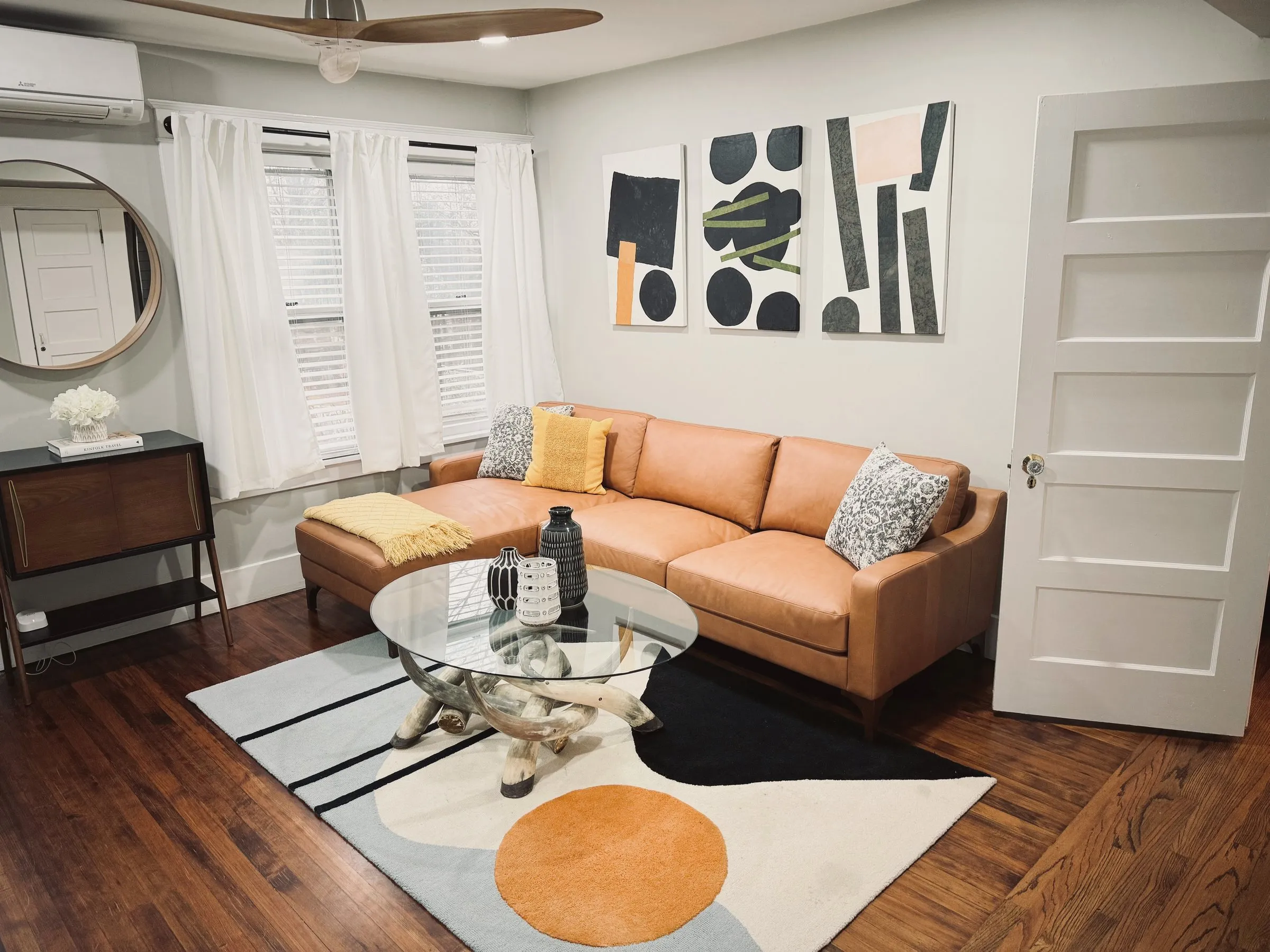 The carriage house living room — leather sofa with chaise, big TV, desk by the window
