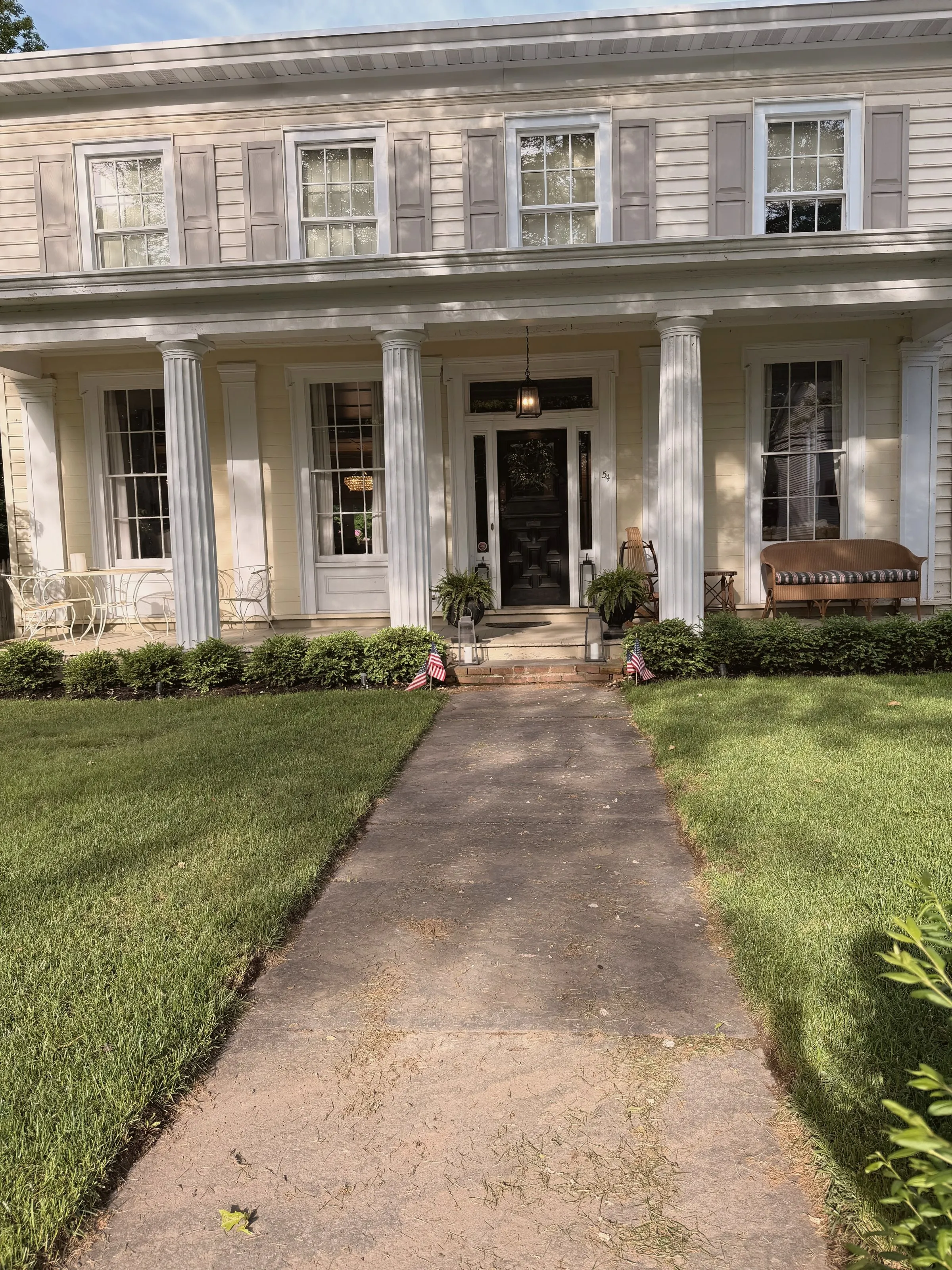The front porch — fluted columns, a wooden swing, ferns by the black front door